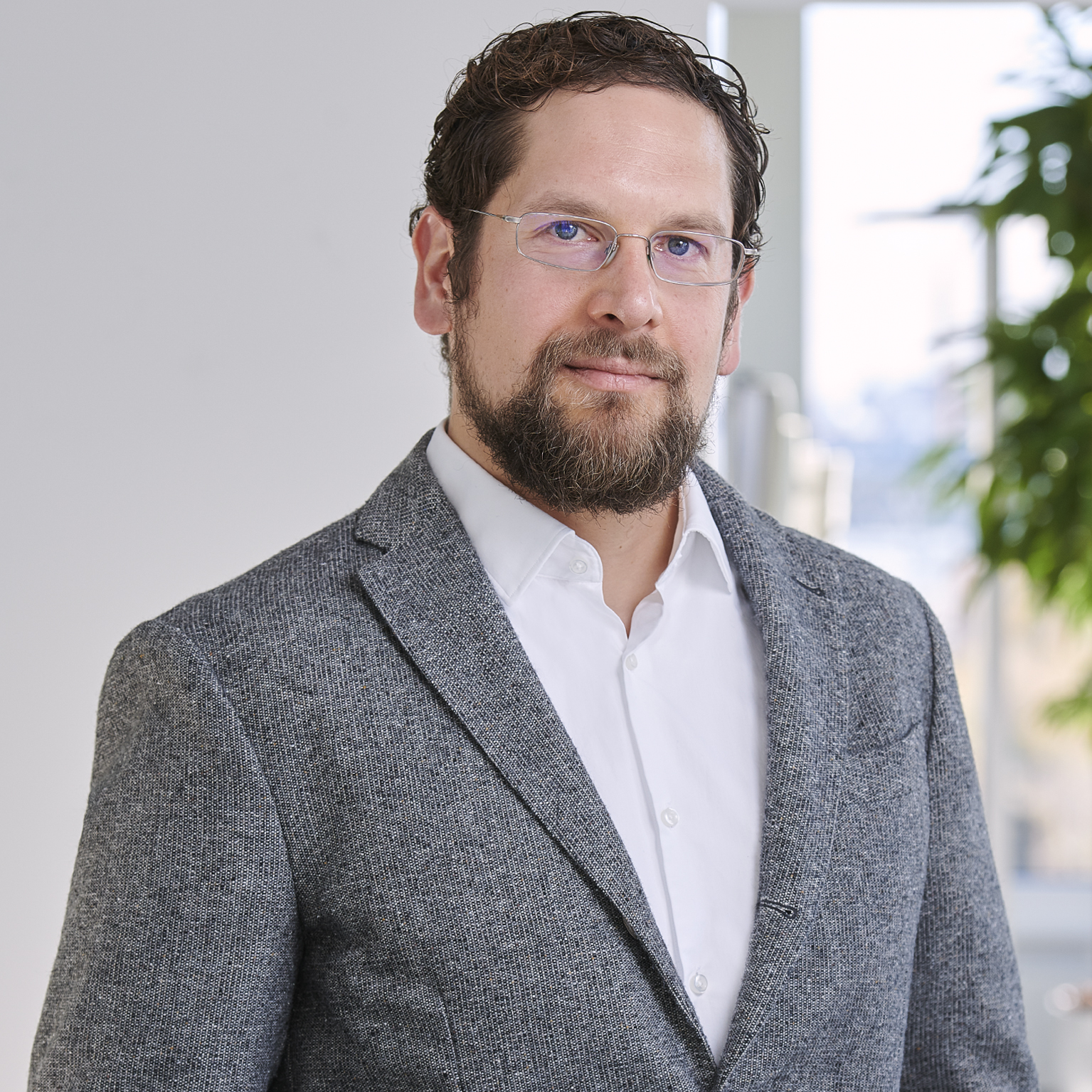 Portrait of Jochen Keil, Patent Professional, wearing a suit and smiling in front of a neutral background with plants.